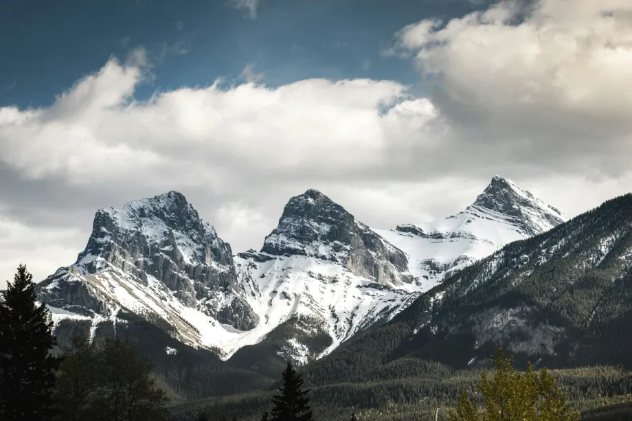 Snow-dusted Three Sisters peaks above Canmore under a cloudy sky